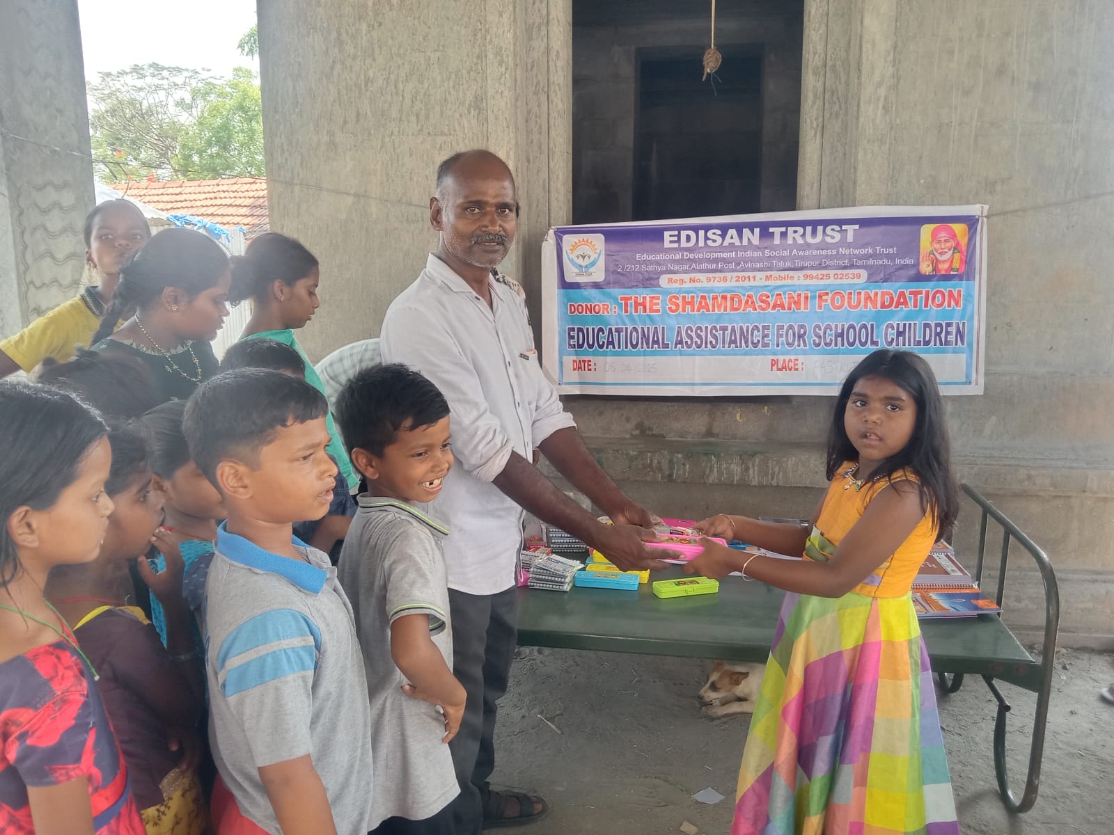 Girl receiving a pink pencil box while other children wait their turn